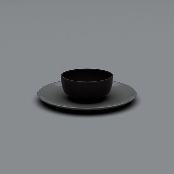 Modern black matte ceramic bowl on grey round plate with smooth finish on grey background